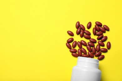 Bottle with pills on yellow background, flat lay. Space for text