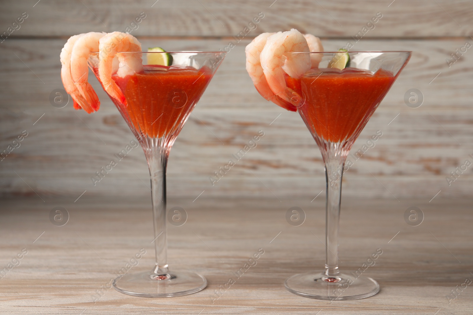 Photo of Tasty shrimp cocktail with sauce and lime in glasses on wooden table