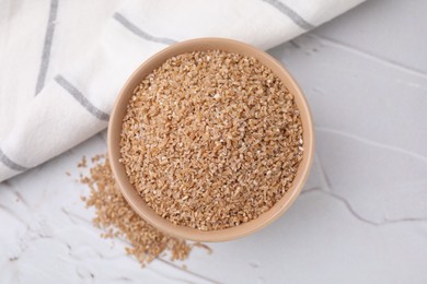 Dry wheat groats in bowl on light textured table, top view