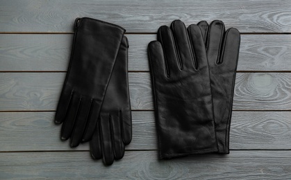 Stylish black leather gloves on grey wooden background, flat lay