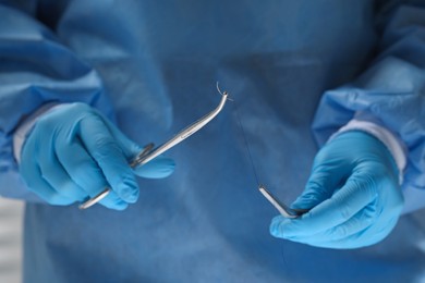 Professional surgeon holding forceps with suture thread, closeup. Medical equipment