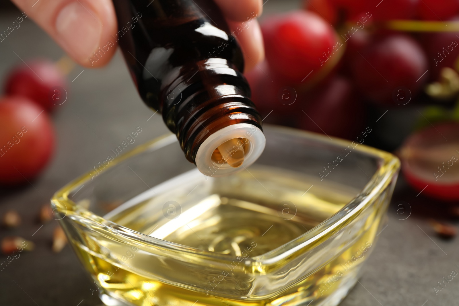 Photo of Woman dripping natural grape seed oil into bowl, closeup. Organic cosmetic