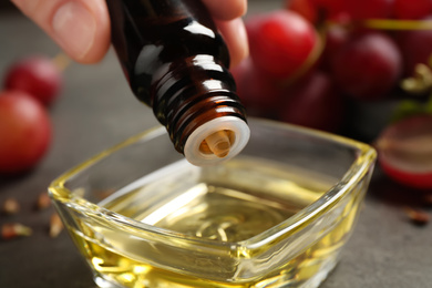 Woman dripping natural grape seed oil into bowl, closeup. Organic cosmetic