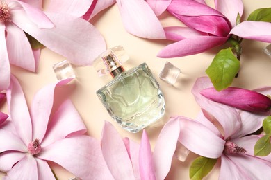 Beautiful pink magnolia flowers, bottle of perfume and ice cubes on beige background, flat lay