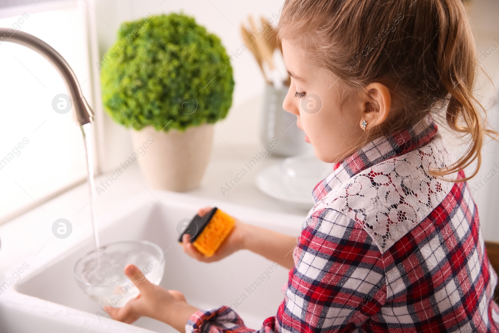 Photo of Little girl washing dishes in kitchen at home