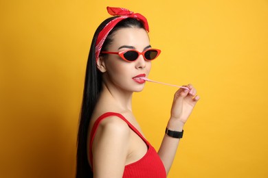 Photo of Fashionable young woman in pin up outfit chewing bubblegum on yellow background