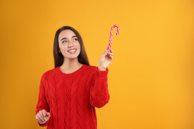 Photo of Young woman in red sweater holding candy cane on yellow background, space for text. Celebrating Christmas