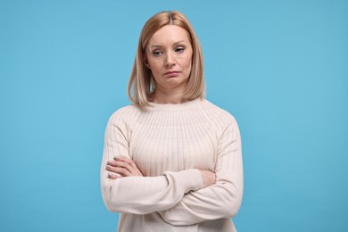Sad woman with crossed arms on light blue background