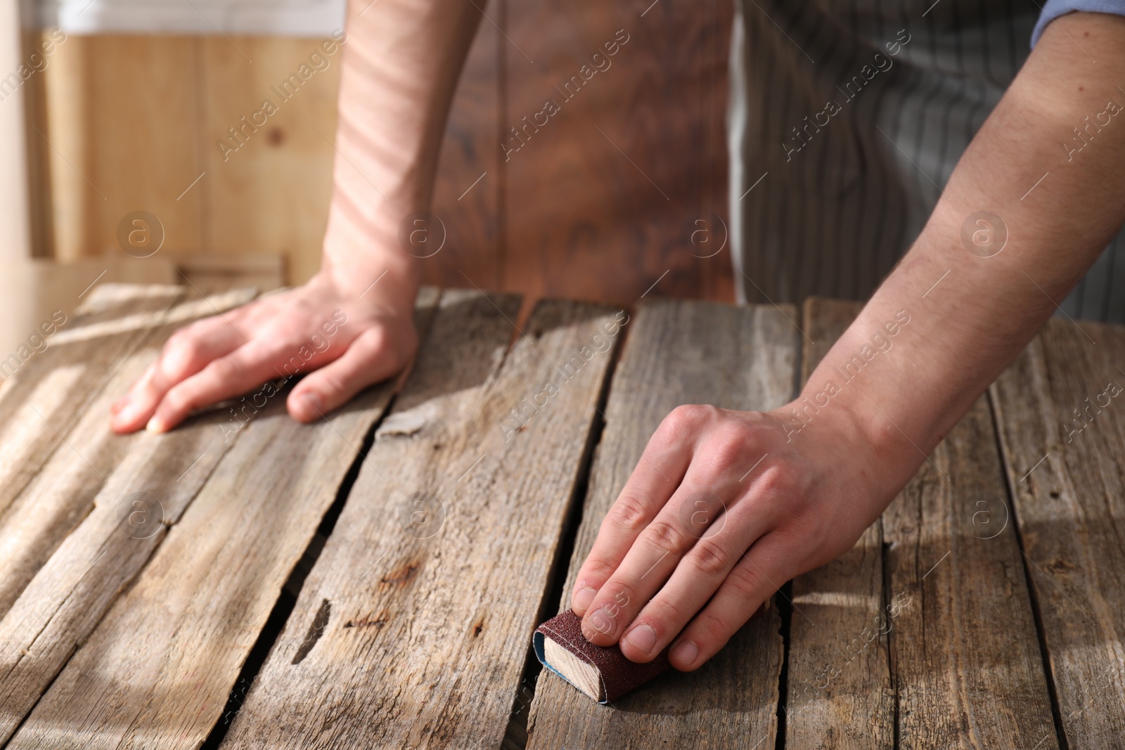 Photo of Man polishing wooden table with sandpaper indoors, closeup