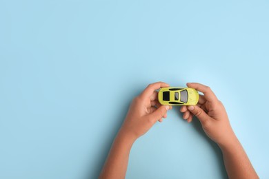Photo of Child holding toy car on light blue background, top view. Space for text