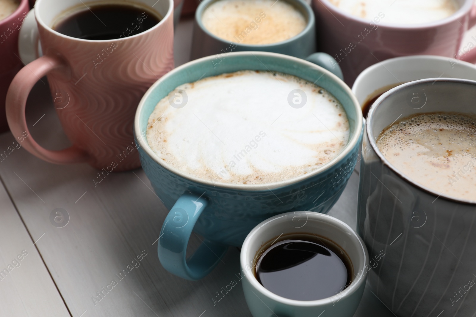 Photo of Many different cups with aromatic hot coffee on white wooden table