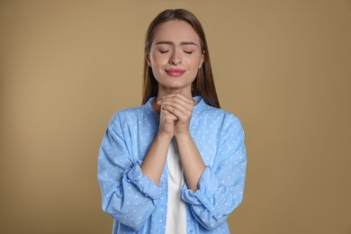 Woman with clasped hands praying on beige background