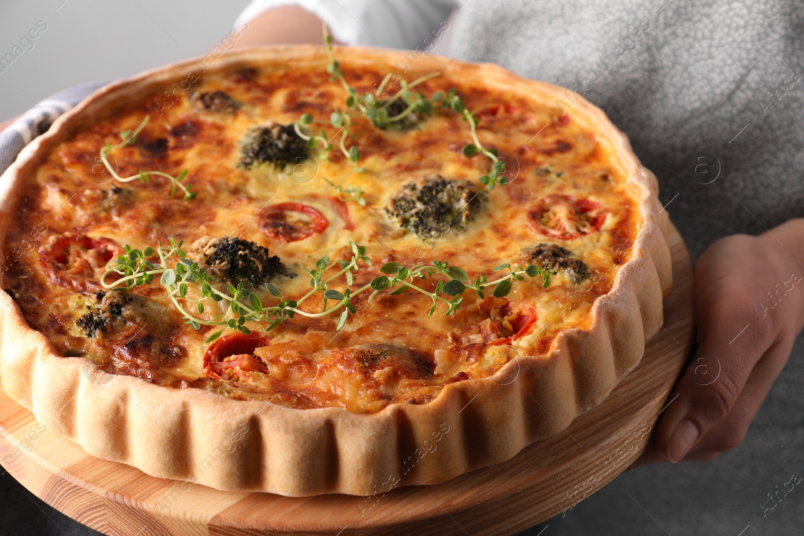 Photo of Woman holding delicious homemade vegetable quiche on light gray background, closeup