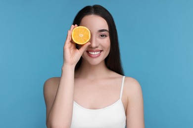 Beautiful young woman with piece of orange on light blue background