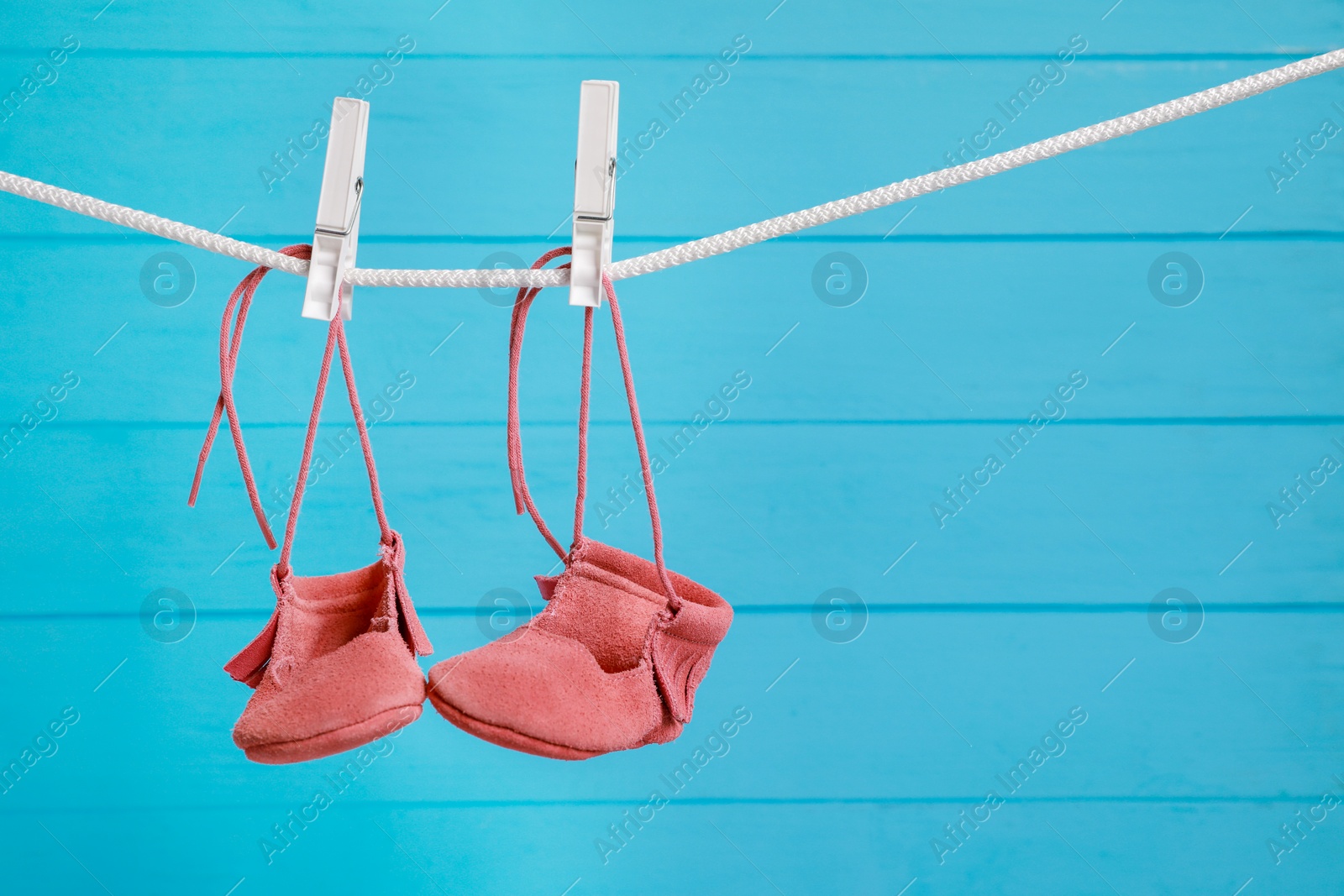 Photo of Pink baby shoes drying on washing line against light blue wooden wall. Space for text