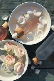 Photo of Bottles of rose essential oil and flowers on light blue wooden table, flat lay