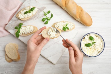 Photo of Woman spreading cottage cheese onto bread at white wooden table, top view