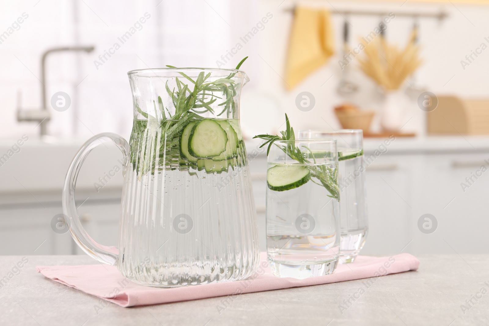 Photo of Refreshing cucumber water with rosemary on table in kitchen