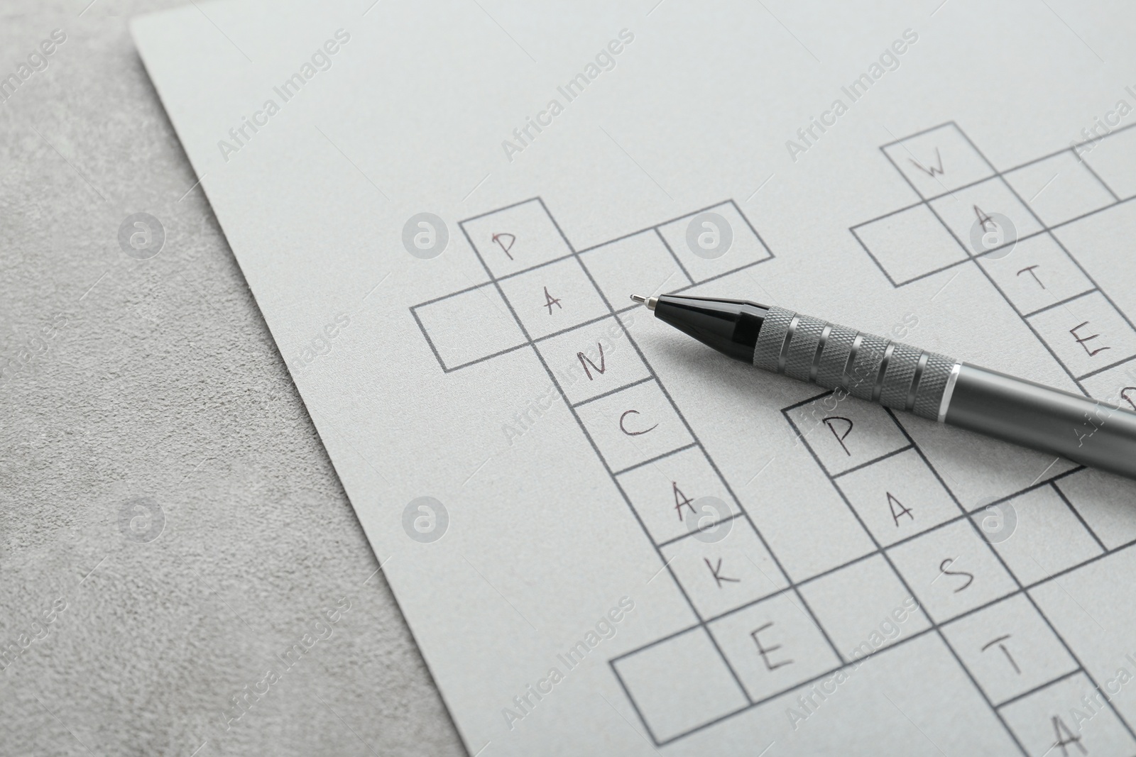 Photo of Crossword with answers and pen on old white table