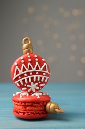 Photo of Beautifully decorated Christmas macarons on light blue wooden table against blurred festive lights