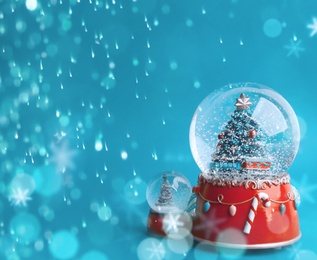 Image of Beautiful snow globes with Christmas trees on blue background, space for text. Bokeh effect