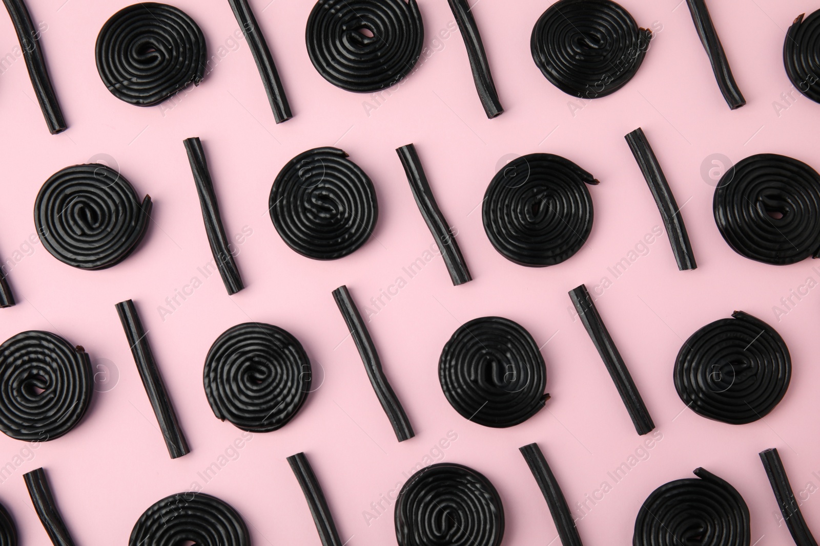 Photo of Tasty black liquorice candies on pink background, flat lay