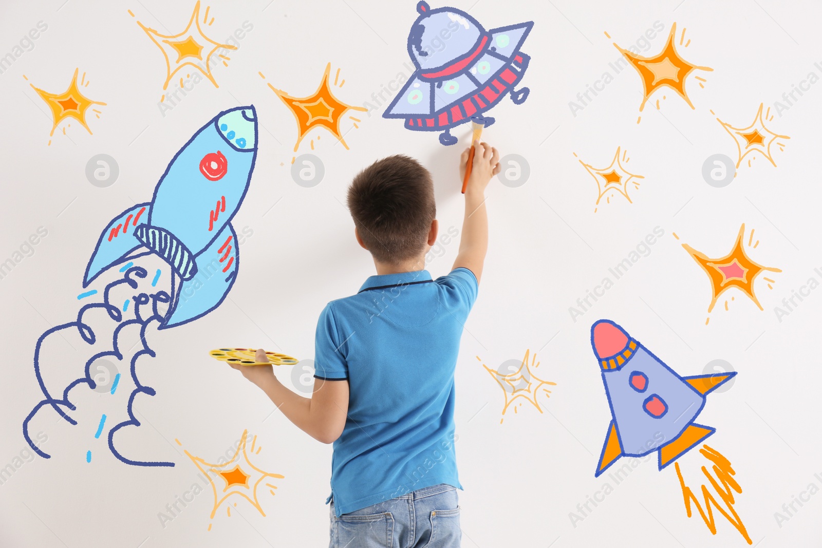 Image of Cute child drawing spaceships on white wall indoors