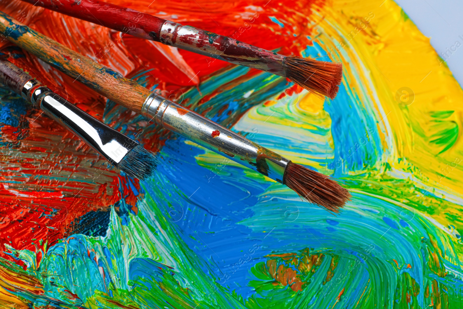 Photo of Closeup view of artist's palette with mixed paints and brushes as background