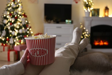 Woman with popcorn watching TV in room decorated for Christmas, closeup