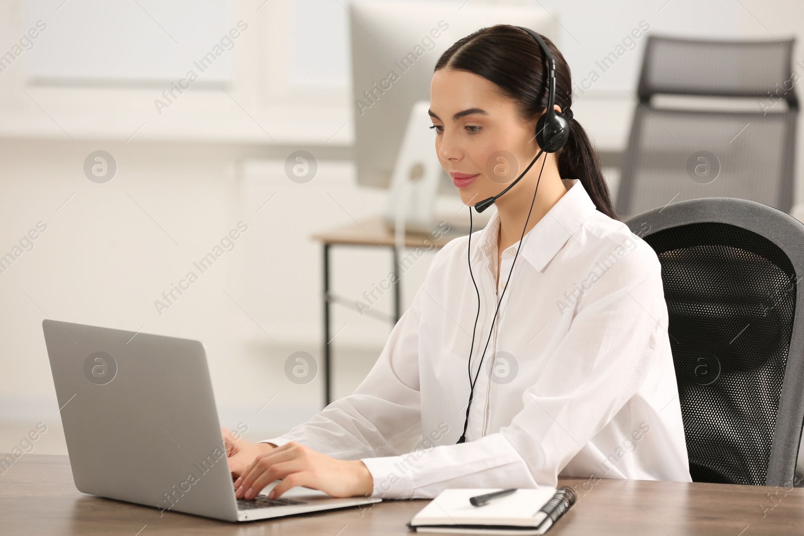 Photo of Hotline operator with headset working on laptop in office