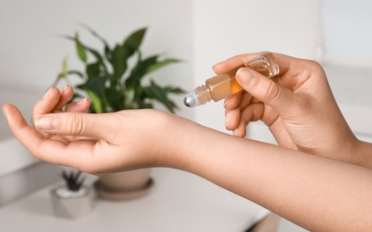 Photo of Woman applying essential oil on wrist indoors, closeup