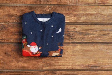 Photo of Warm folded Christmas sweater on wooden table, top view. Space for text