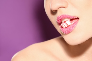 Photo of Beautiful young woman holding candy in lips covered with sugar on color background