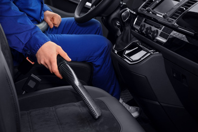 Photo of Car wash worker vacuuming automobile seat, closeup