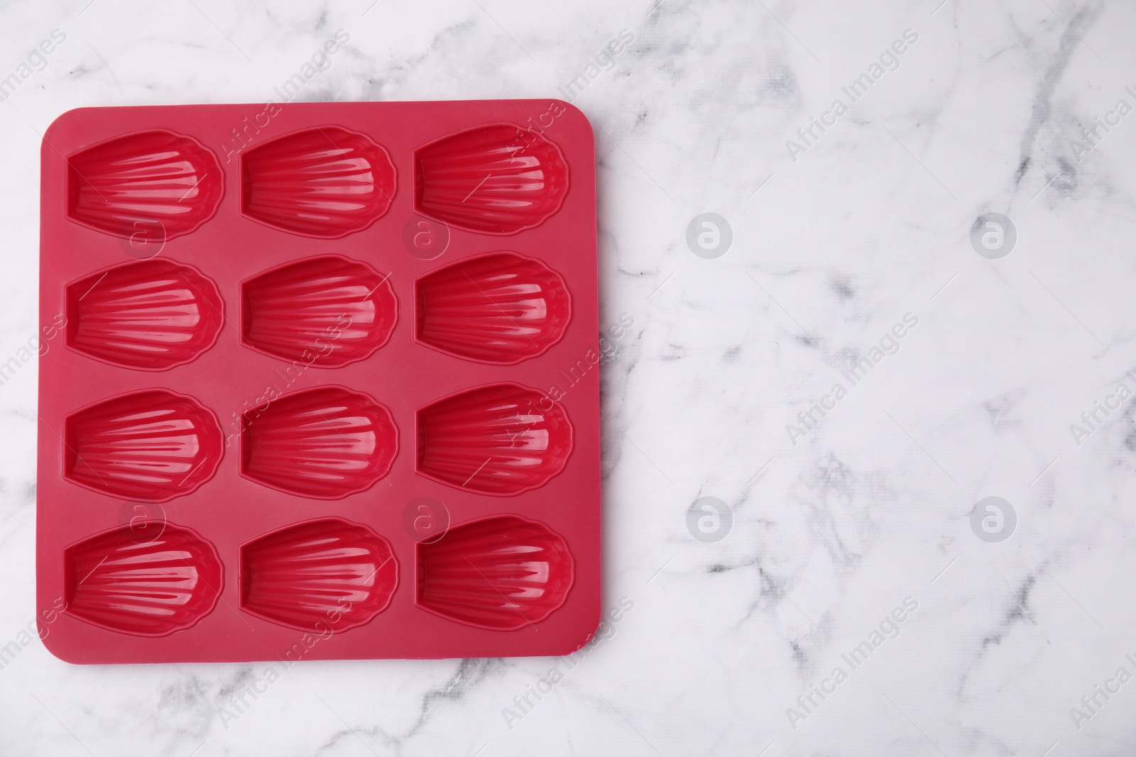 Photo of Red baking mold for madeleine cookies on white marble table, top view. Space for text