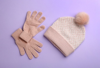 Woolen gloves and hat on violet background, flat lay