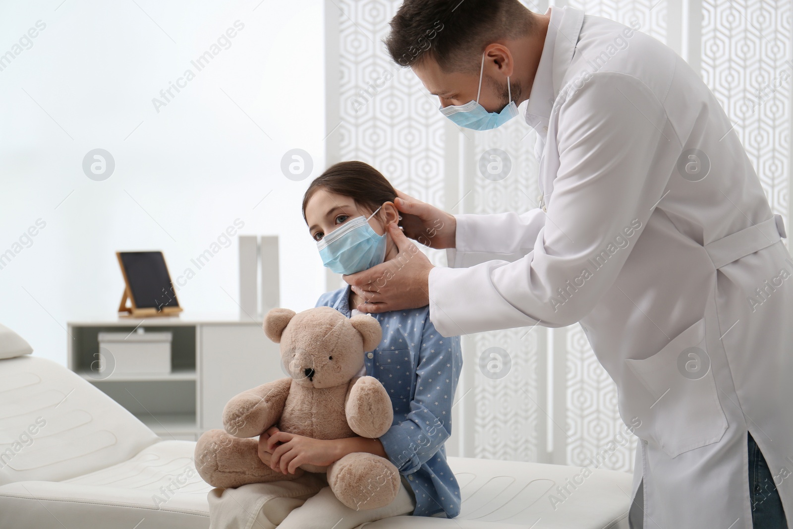 Photo of Pediatrician examining little girl in hospital. Doctor and patient wearing protective masks