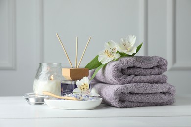 Photo of Spa composition. Towels, burning candles, reed air freshener, sea salt and beautiful flowers on white wooden table