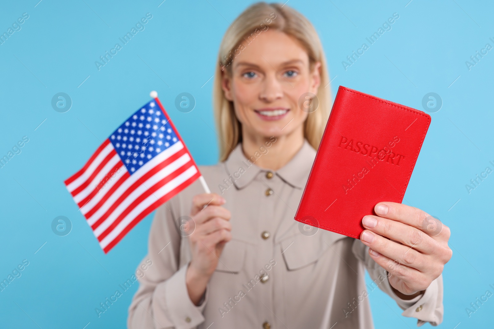 Photo of Immigration. Happy woman with passport and American flag on light blue background, selective focus