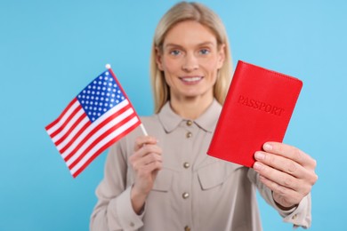 Immigration. Happy woman with passport and American flag on light blue background, selective focus
