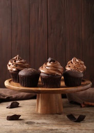 Photo of Delicious chocolate muffins and cupcakes decorated with cream on wooden table