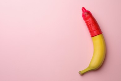 Banana with condom on pink background, top view and space for text. Safe sex concept