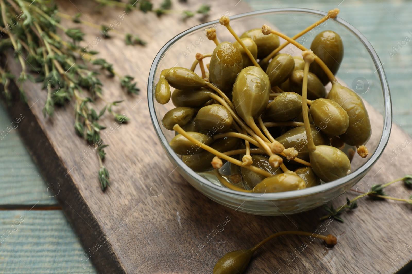 Photo of Tasty capers in glass bowl and thyme on light blue table, closeup