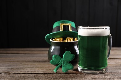 Photo of St. Patrick's day celebration. Green beer, leprechaun hat, pot of gold and decorative clover leaf on wooden table. Space for text