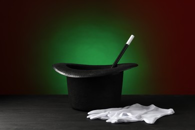 Photo of Magician's hat, wand and gloves on black wooden table against dark background