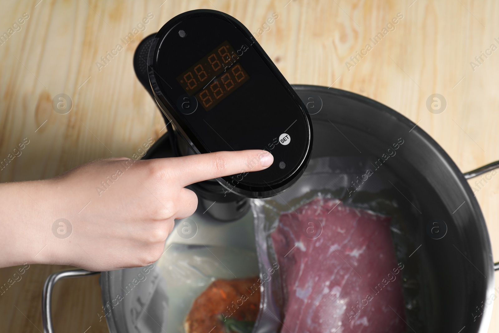 Photo of Woman using thermal immersion circulator at wooden table, closeup. Sous vide, cooking meat in vacuum packing