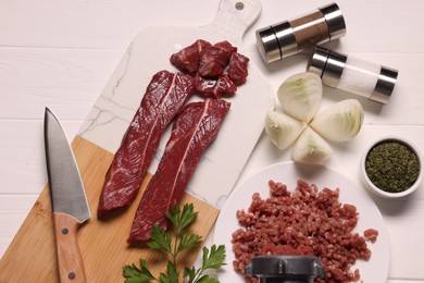 Photo of Manual meat grinder with beef, onion and spices on white wooden table, flat lay