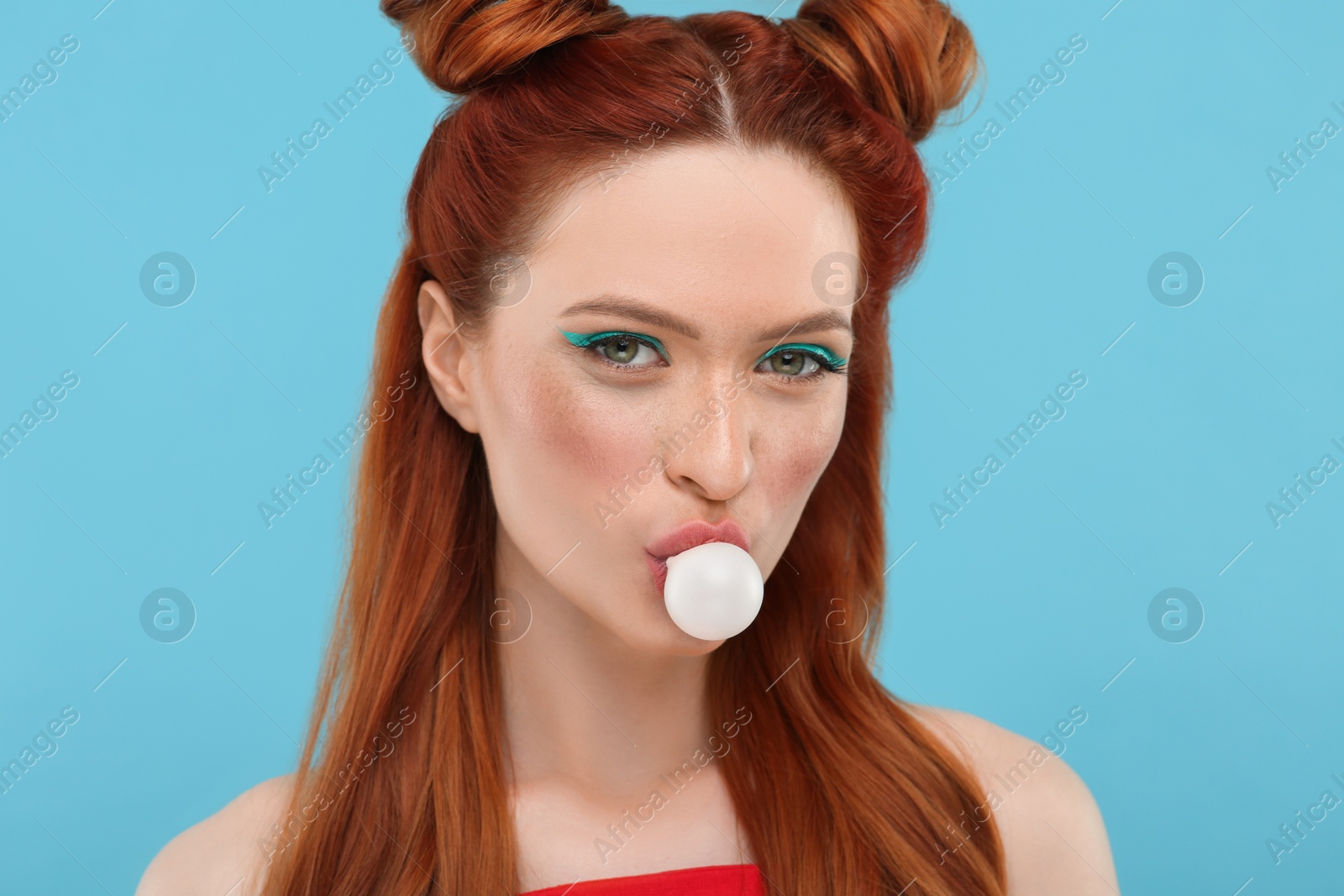 Photo of Portrait of beautiful woman with bright makeup blowing bubble gum on light blue background