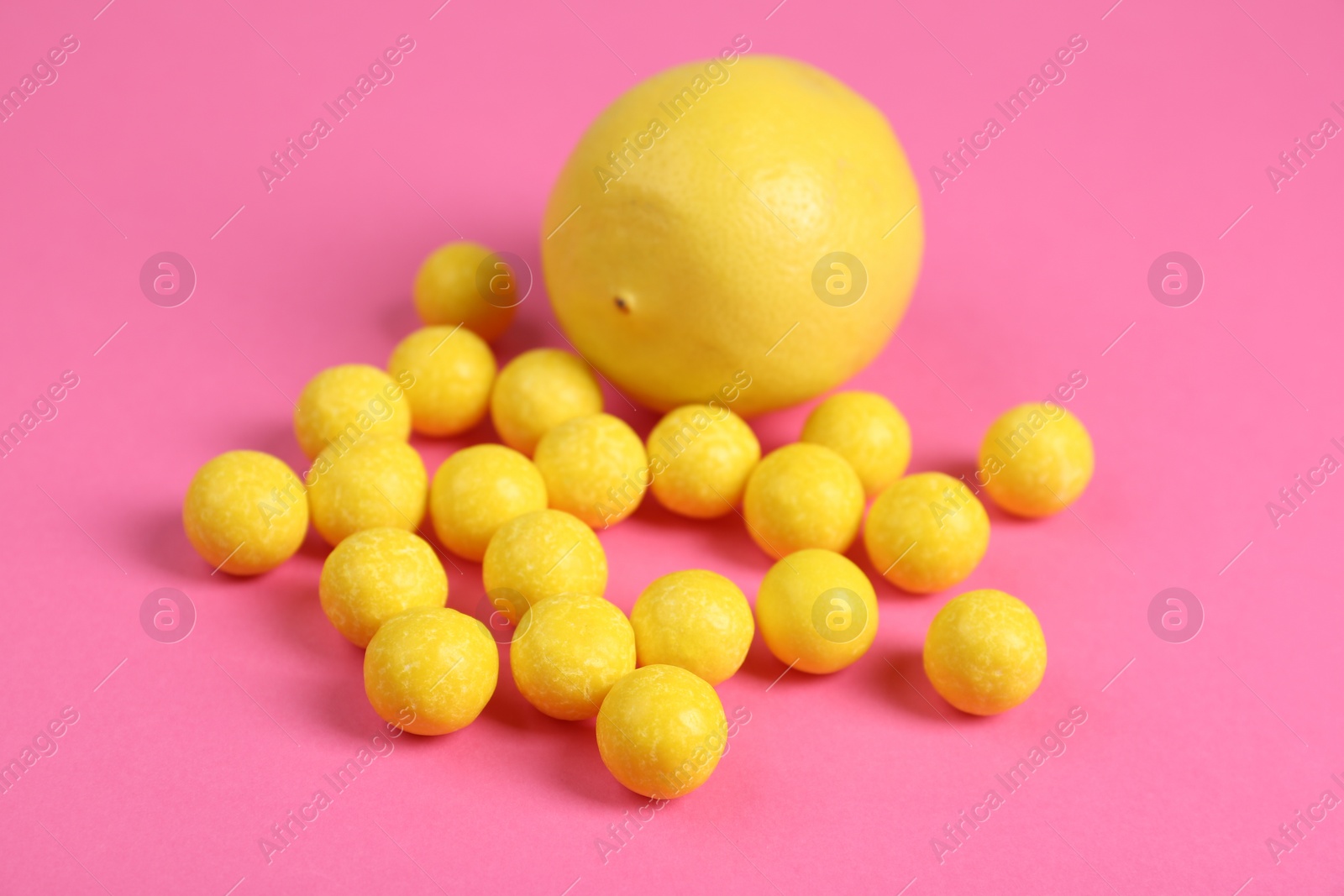 Photo of Whole fresh lemon and yellow candies on pink background