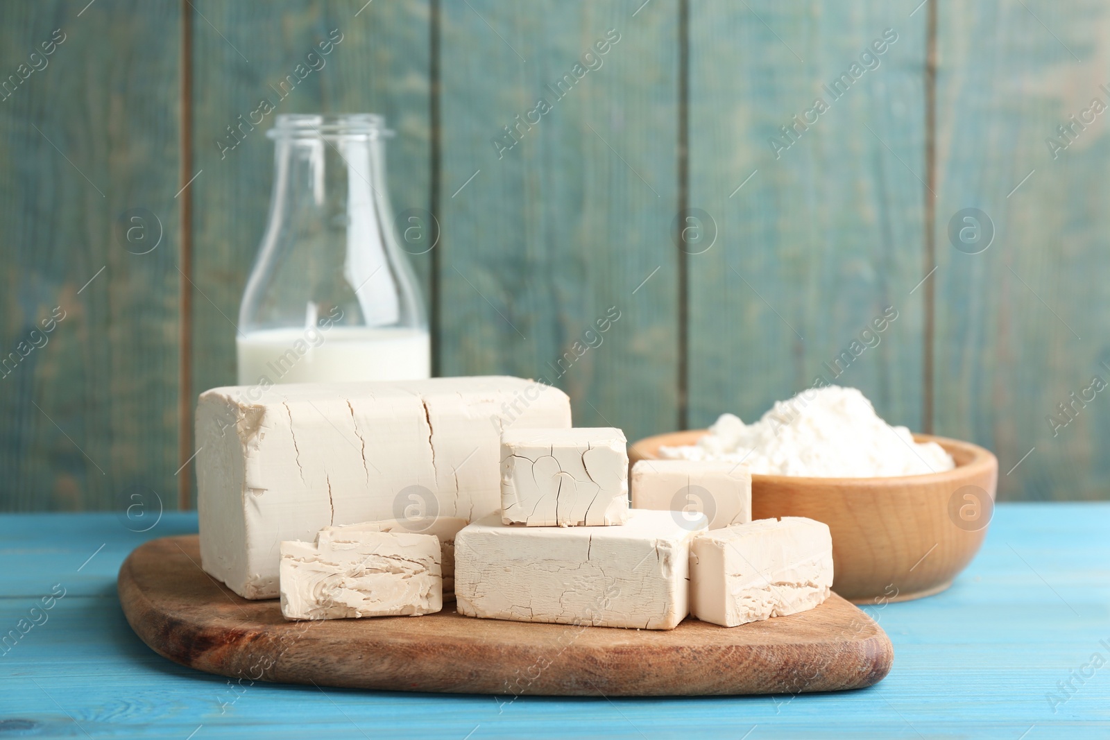 Photo of Pieces of compressed yeast near ingredients for dough on light blue wooden table